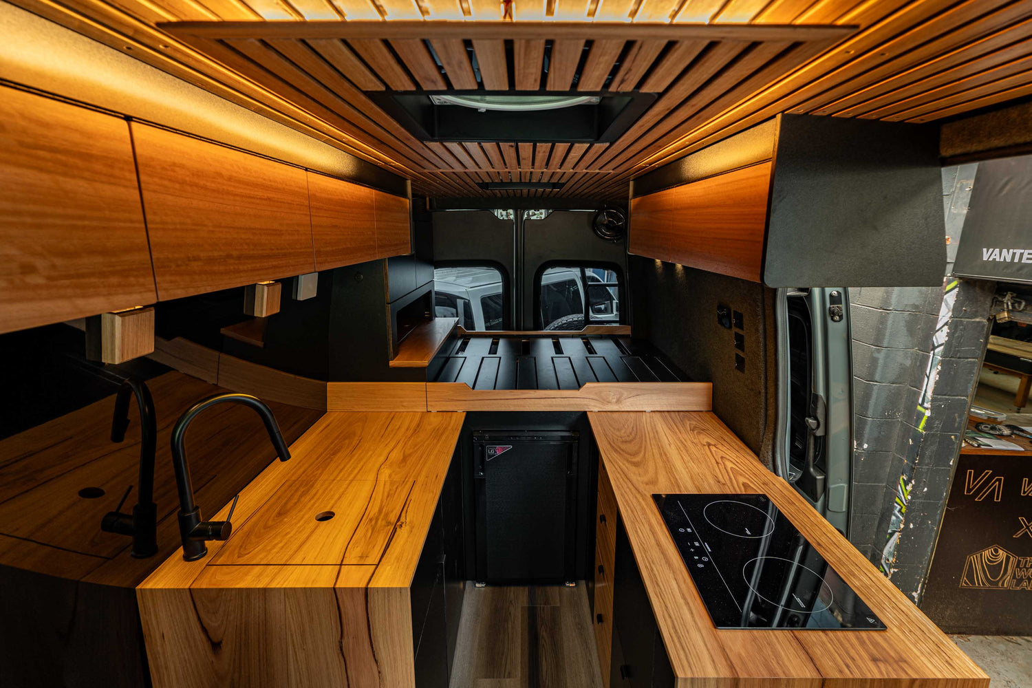 Interior of Matt's Mercedes Sprinter 4x4 van conversion by Vanted Sydney, featuring black butt timber benchtop, induction cooktop, sink and mood lighting