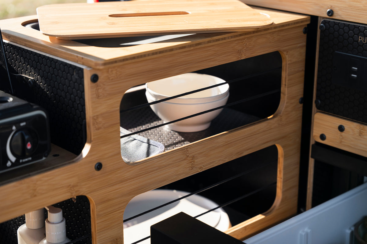 Close-up of a bamboo kitchen organizer or storage unit with open shelves, a white bowl inside, and a matching bamboo lid resting on top.
